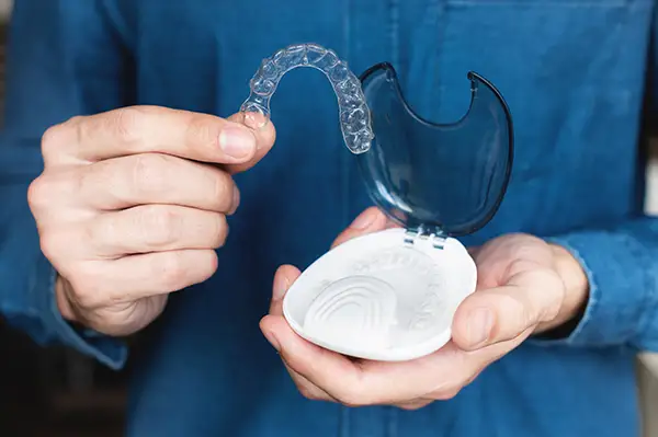 Hands holding a clear aligner and its storage case, emphasizing care and convenience for adult orthodontic treatment. Hands holding a clear aligner and its storage case, emphasizing care and convenience for adult orthodontic treatment.