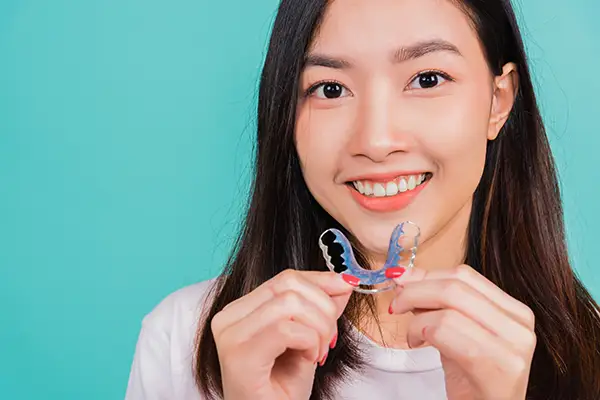 Happy young woman holding a colorful orthodontic retainer, emphasizing post-treatment care. Happy young woman holding a colorful orthodontic retainer, emphasizing post-treatment care.