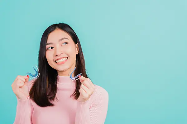 Young smiling woman holding clear retainers, encouraging their use after orthodontic treatment. Young smiling woman holding clear retainers, encouraging their use after orthodontic treatment.