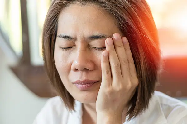 A woman holding her jaw in discomfort, showing symptoms of TMJ pain with a look of distress. A woman holding her jaw in discomfort, showing symptoms of TMJ pain with a look of distress.