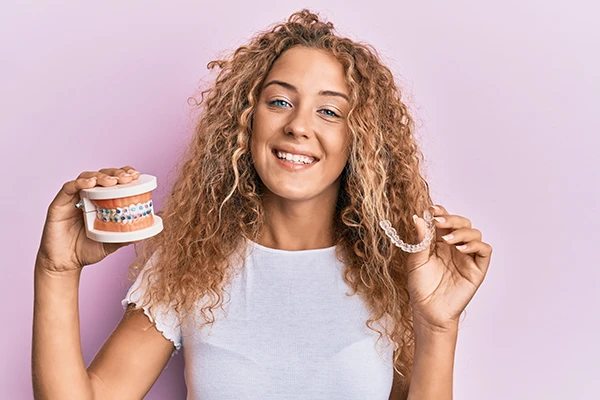 A girls holding braces model in one hand and clear aligners in other. A girls holding braces model in one hand and clear aligners in other.