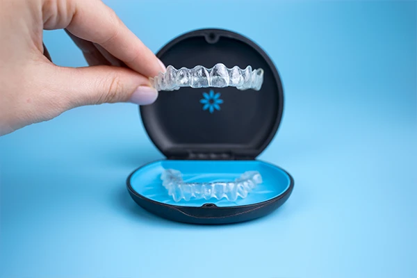 A hand holding Invisalign aligner over the aligner's case A hand holding Invisalign aligner over the aligner's case