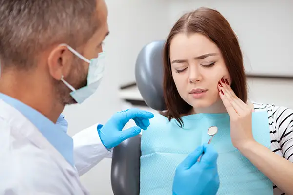 Female patient in a dental chair, holding her jaw and describing an orthodontic problem to a dentist during an emergency appointment. Female patient in a dental chair, holding her jaw and describing an orthodontic problem to a dentist during an emergency appointment.