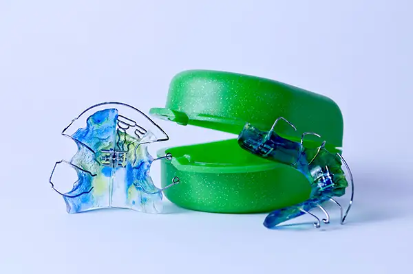 Two colorful wire and plastic retainers placed next to a retainer case on a white background. Two colorful wire and plastic retainers placed next to a retainer case on a white background.